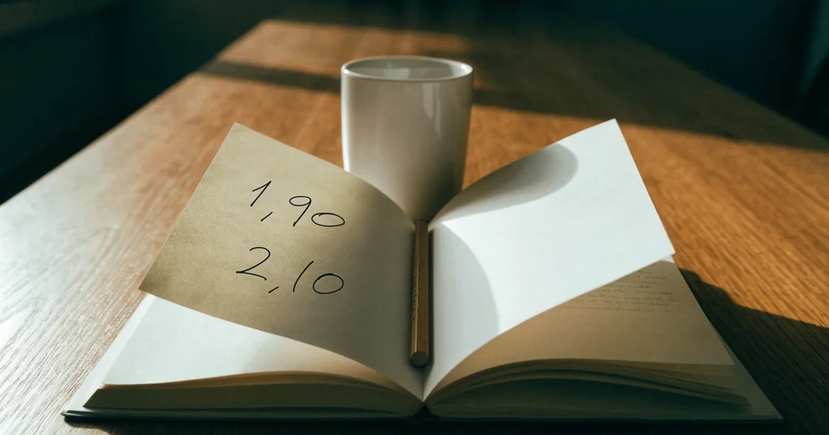 Um caderno aberto com cotas escritas à mão, uma calculadora e um lápis sobre uma mesa de madeira